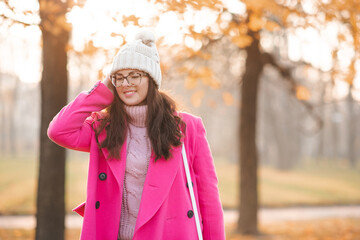 Happy stylish woman wear pink autumn jacket and knitted hat walk on city street outdoor. Fall...