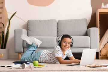 Little African-American boy in headphones with laptop studying computer sciences online at home