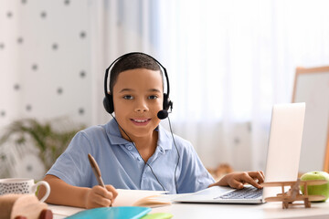 Little African-American boy in headset studying computer sciences online at home