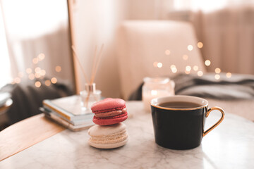 Fototapeta na wymiar Cup of coffee with macarons and stack of paper books with candle on marble table in bedroom top view closeup.