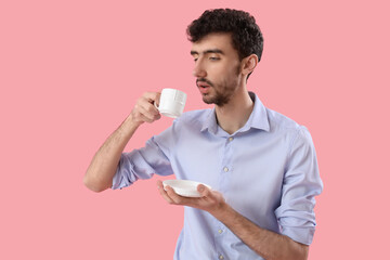 Young businessman with cup of coffee on pink background