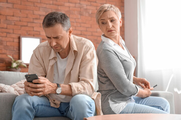 Offended mature couple using mobile phones after quarrel at home