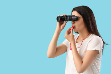 Female lifeguard with binoculars whistling on blue background