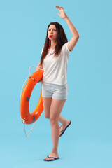 Female lifeguard with ring buoy whistling on blue background