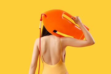 Female lifeguard with board on yellow background, back view