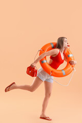 Fototapeta na wymiar Female lifeguard with ring buoy, whistle and first aid kit running on beige background