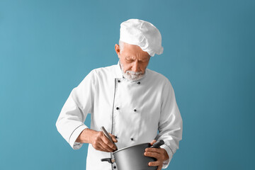 Mature chef with cooking pot on blue background