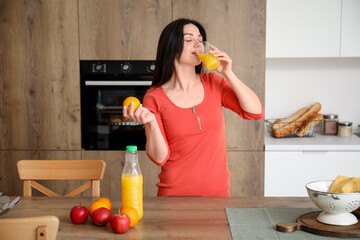 Beautiful woman with orange drinking juice in kitchen