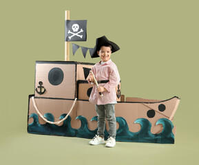 Cute little pirate with spyglass and cardboard ship on green background