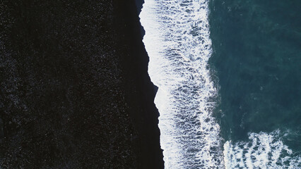 Icelandic black sand beach aerial view, spectacular atlantic shore with waves crashing on coastline. Arctic scenery with snowy mountains and black sand on beaches, cold landscape. Slow motion.