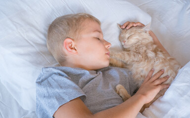 the boy falls asleep and hugs his ginger cat, who sleeps with him under the covers. children and pets. the cat sleeps with the baby. the child is getting ready for bed.