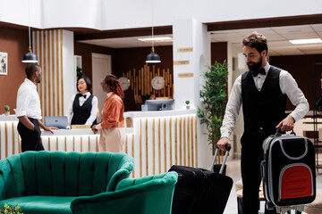 Hotel bellboy carrying bags for guests, helping tourists to find room after doing check in...