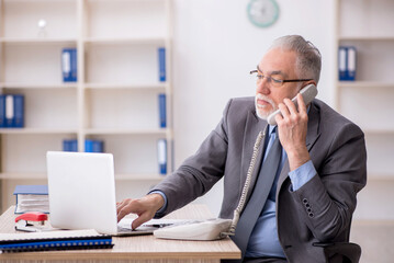 Naklejka premium Old male employee speaking by phone at workplace