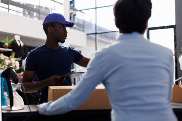 Obraz premium African american courier explaining shipping details to worker, taking cardbord boxes from counter desk in shopping mall. Manager preparing packages for delivery, working in modern boutique