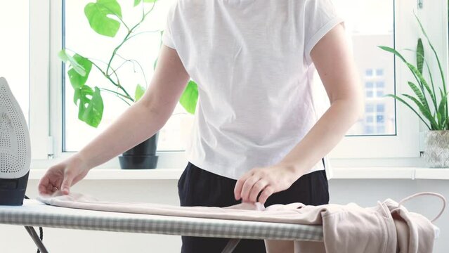 Woman ironing light pink hoodie on ironing board. Hot stem from iron. Female hand holding electric iron, household chores. Home routine housekeeping. High quality 4k footage