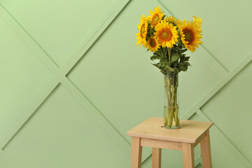 Vase with beautiful sunflowers on stool near green wall in room