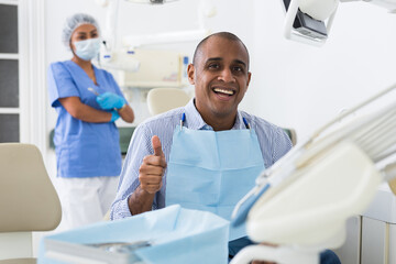 Happy man sitting in dental chair after teeth cure