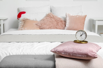 Soft bench with alarm clock, pillow and plaid in light bedroom