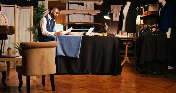 Male tailor checking sketches in atelier, using outline drawings of clothing items before designing luxury fashion collection. Couturier manufacturing custom made clothes, small business.