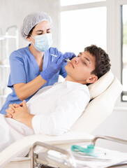 Obraz premium Female doctor conducting face revitalization procedure for young man patient by micro-injection method