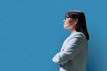 Serious mature business woman, profile view on blue studio background