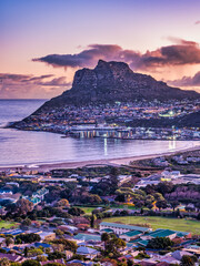 Fototapeta premium Aerial vertical shot of Hout Bay town, harbour, mountain and the beach during sunset, Western Cape, South Africa