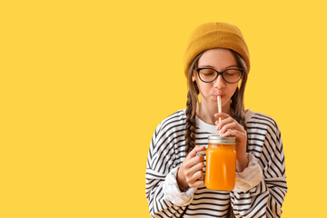 Little girl drinking juice on yellow background