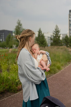 Woman carrying and kissing baby in park against sky