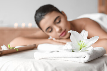 Fototapeta na wymiar Lily flower with bath towel and spa stones near relaxing woman in salon