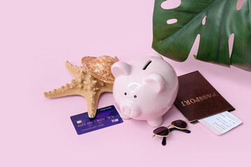 Piggy bank with beach accessories, credit card and passport on pink background. Concept of savings...