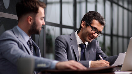 Two men discuss a project while looking at a computer monitor in a modern office.