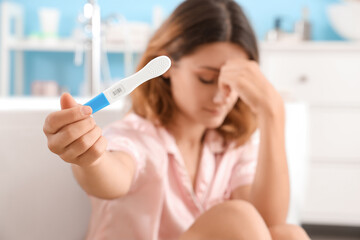 Upset young woman with positive pregnancy test in bathroom, closeup