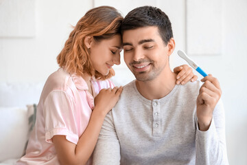 Happy young couple with pregnancy test in bedroom