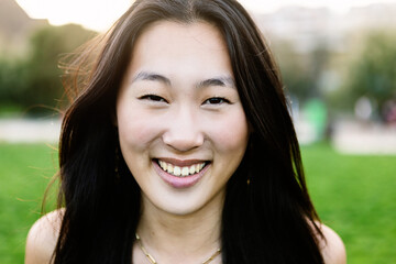 Close up portrait of young asian woman smile outdoors. Happy millennial chinese female looking at camera standing at city park.