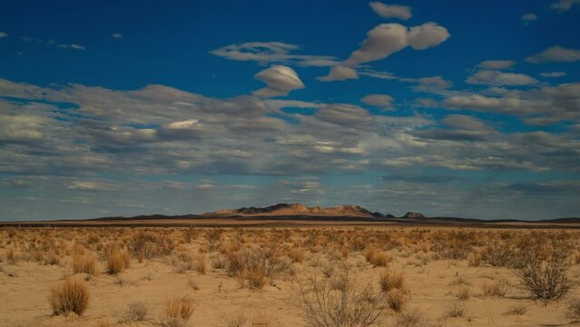 Time lapse of scattered clouds moving over a wide desert plain and distant mountains