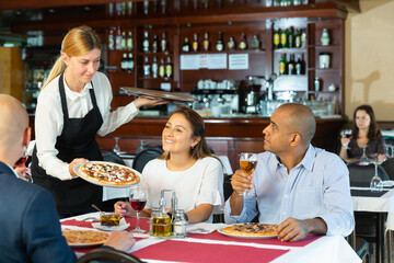 Fototapeta na wymiar Helpful waitress brought delicious pizza to restaurant guests