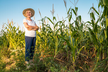 Happy senior woman with hat standing next to her organic corn field