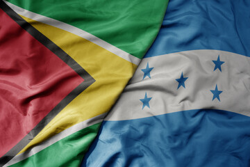 big waving realistic national colorful flag of guyana and national flag of honduras .