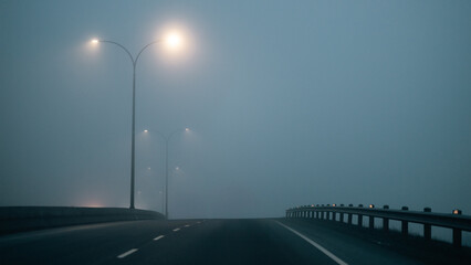 Eerie view of night foggy highway dimly lit by street lights.