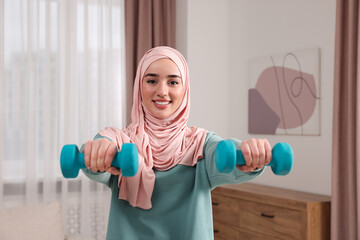 Fototapeta na wymiar Muslim woman in hijab doing exercise with dumbbells at home
