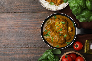 Delicious chicken with curry sauce and ingredients on wooden table, flat lay. Space for text