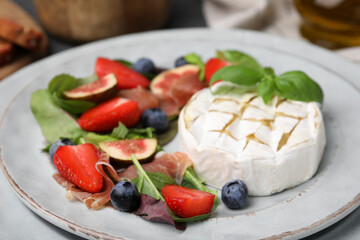 Delicious salad with brie cheese, prosciutto, strawberries and blueberries on plate, closeup