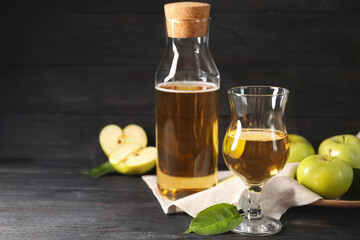 Delicious cider and apples with green leaves on black wooden table, space for text
