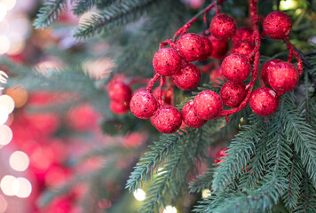 Christmas red ornaments hang on tree, with bokeh background.