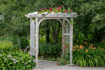 An outdoor wooden curved shaped archway or arbor surrounded by a lush green garden.  The park has...