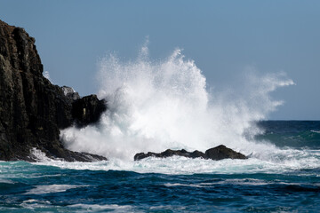 A large teal green color massive rip curl wave as it reaches the rocky shore. There's white frothy...