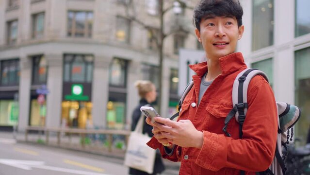 Asian young man backpacker chatting on phone while walking on the city.