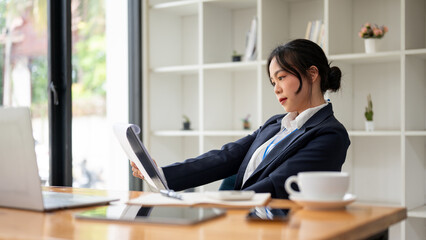 A focused and professional Asian businesswoman is examining a business report in her office.