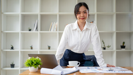 An attractive Asian businesswoman smiling at the camera while standing at her desk.