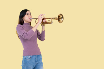A talented and beautiful Asian woman is playing a trumpet, isolated yellow background